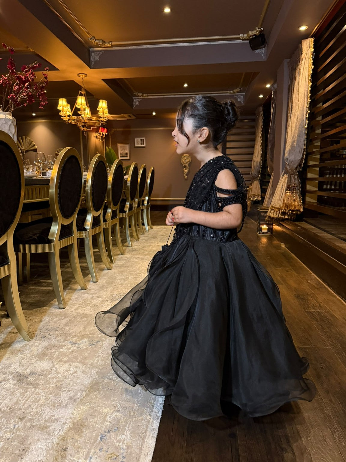 Celeste black gown in side profile, showing beaded arm detailing and flowing organza skirt