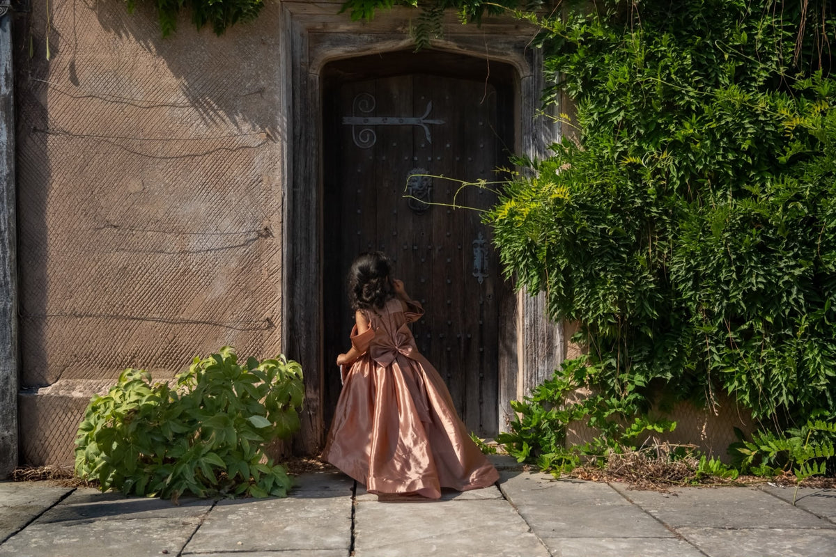 Rosalie rose-gold gown photographed at a stone doorway