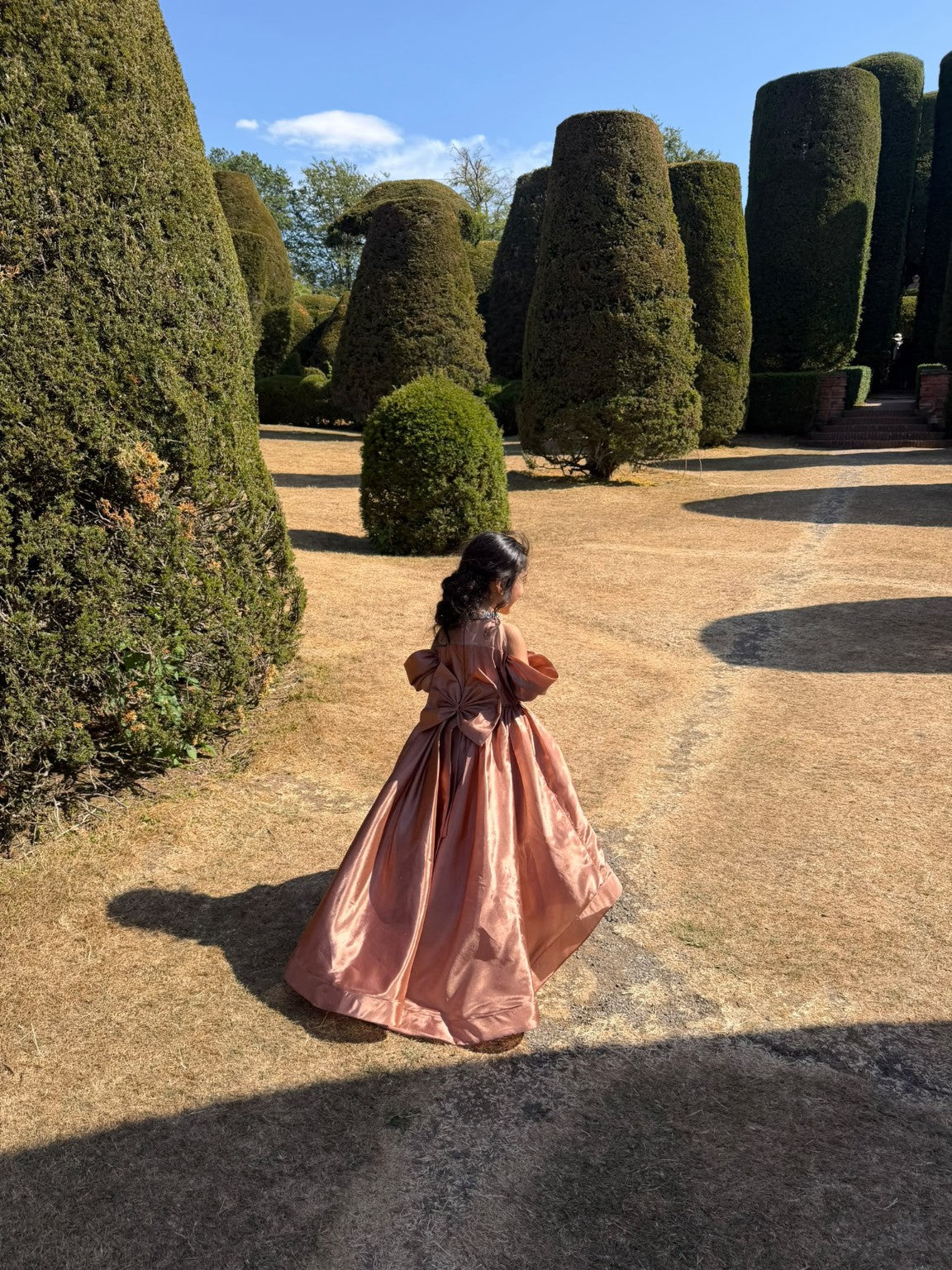 Rosalie rose-gold gown photographed among sculpted garden hedges
