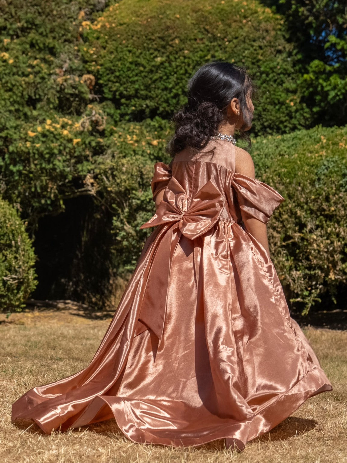 Rosalie rose-gold gown in the garden, showing the detachable bow and flowing trailing skirt