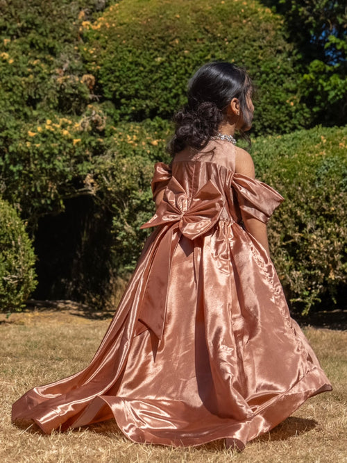 Rosalie rose-gold gown in the garden, showing the detachable bow and flowing trailing skirt