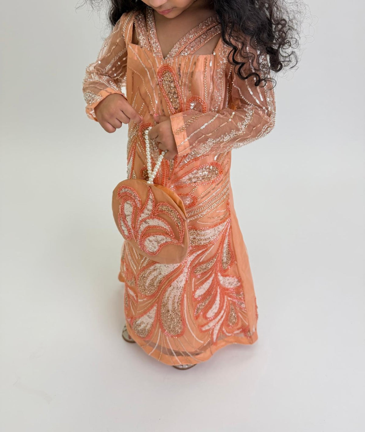 Detail of Zaria’s sheer embellished sleeve and shimmering peach dress; styling pouch is not included